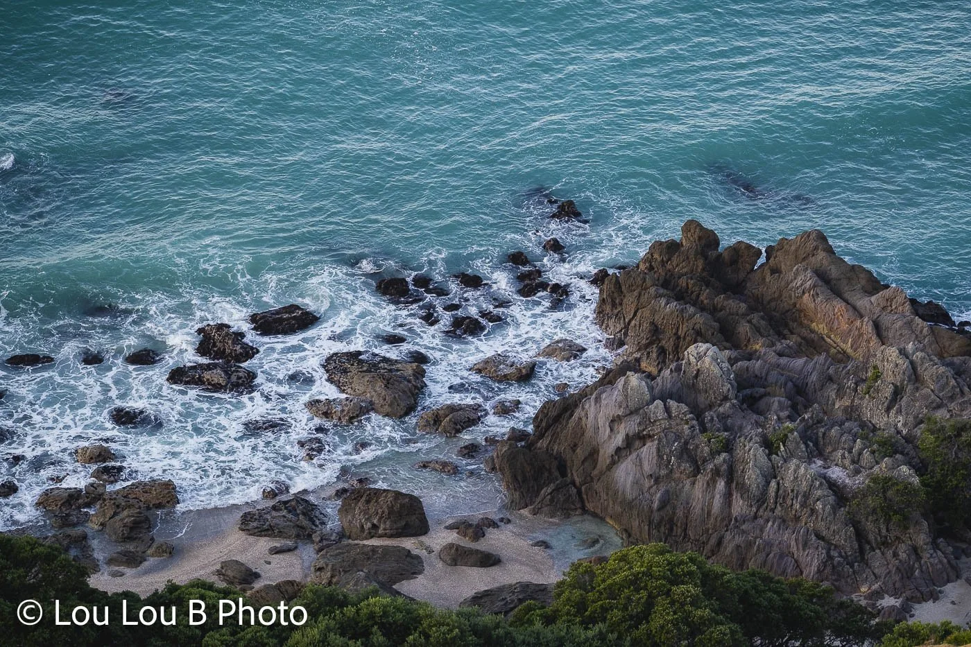 Elevated view of turquoise water washing around a rugged rocky shoreline.