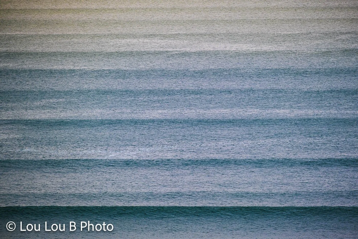 Minimal view of parallel blue ocean swell lines creating repeating bands across the sea.