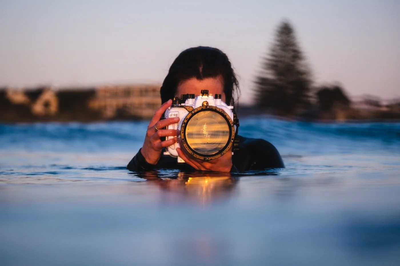 In-water surf photographer using a waterproof camera housing at water level during golden hour