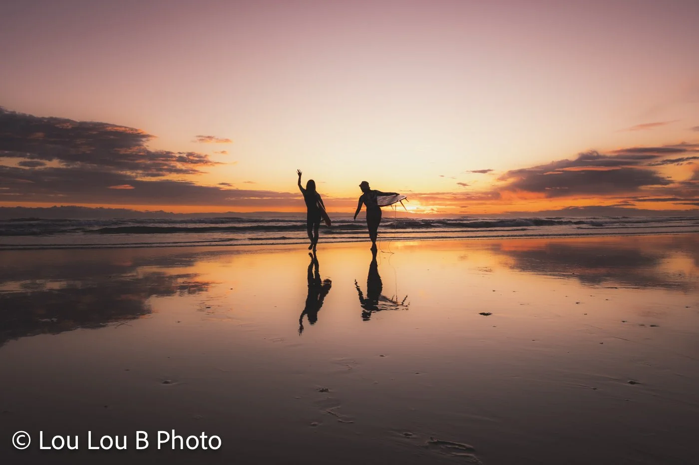 Surfers walking across Mount Maunganui beach at sunset reflected in wet sand