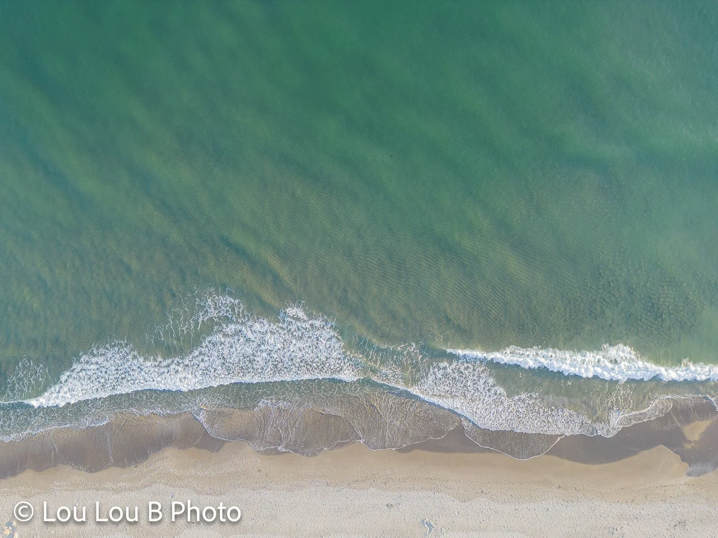 Aerial view of turquoise waves breaking onto a pale sandy beach.