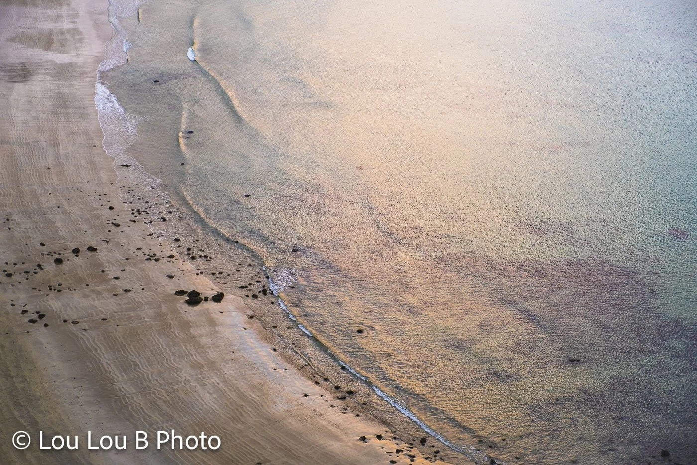 Aerial view of a sweeping sandy coastline washed in soft blush, cream and champagne tones.