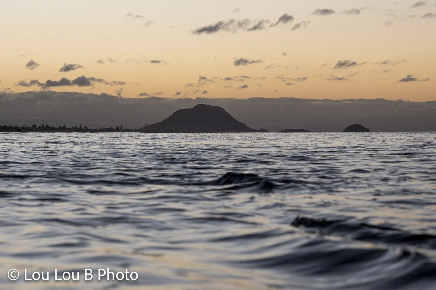 Mount Maunganui silhouetted on the horizon beyond rippled ocean water at golden hour.