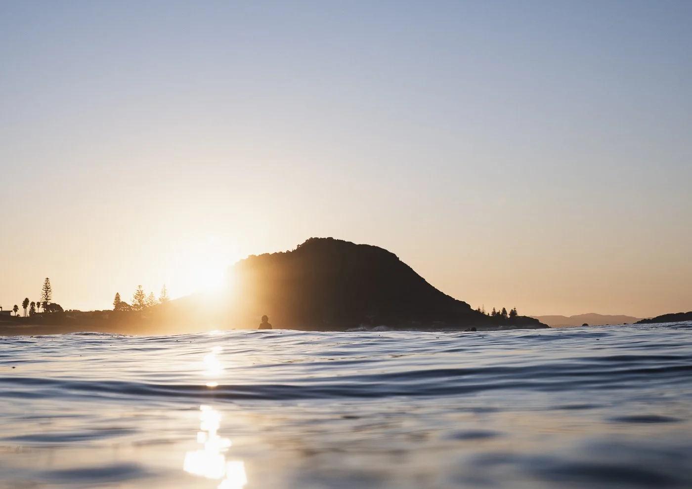 Golden sunrise behind Mauao, Mount Maunganui, with gentle ocean ripples reflecting the morning light.