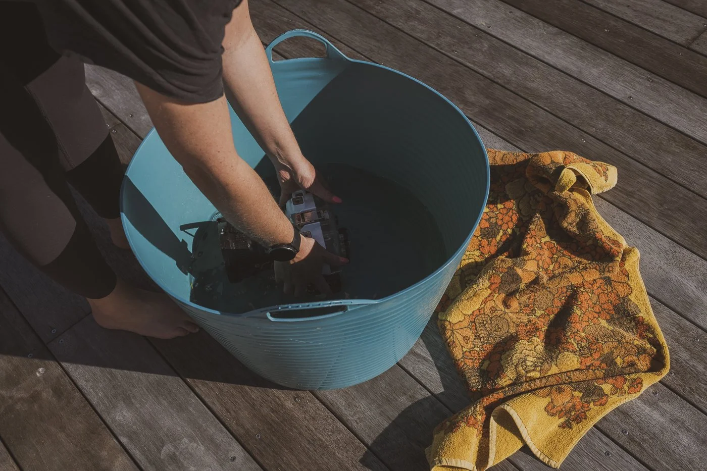 Underwater camera housing being rinsed in fresh water beside a towel after a surf photography session.