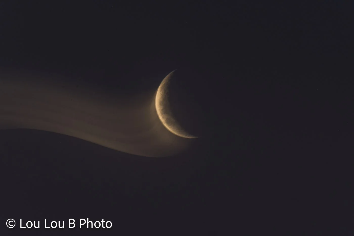 Golden crescent moon setting behind a softly silhouetted coastal landscape at twilight.