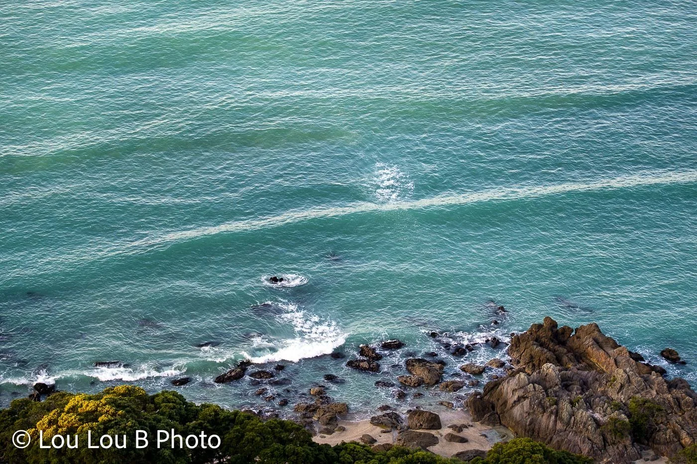 Aerial view of vivid turquoise ocean water meeting a rocky coastline.