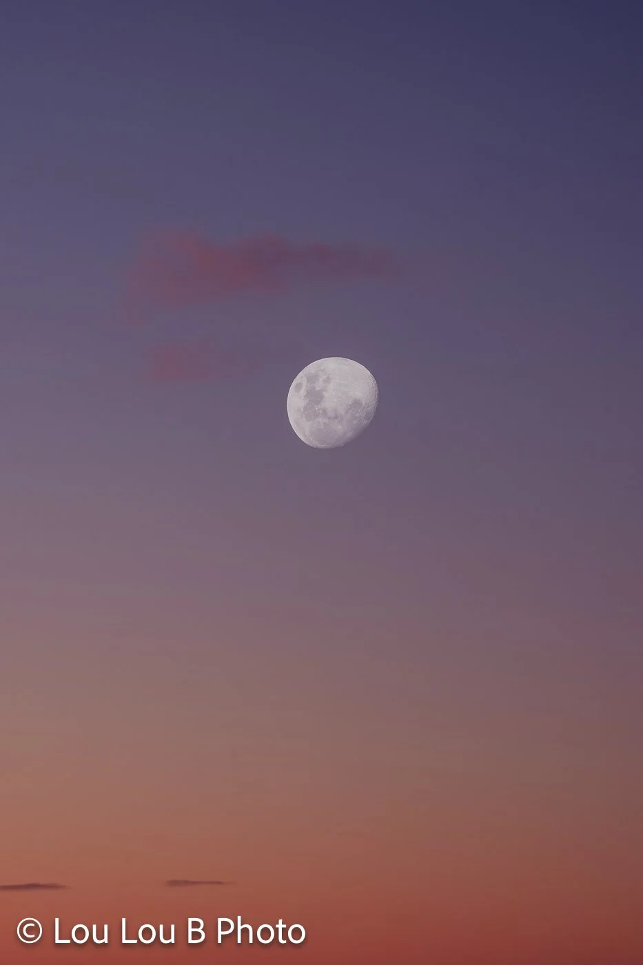 Full moon in a pink, purple and orange gradient sky at twilight.