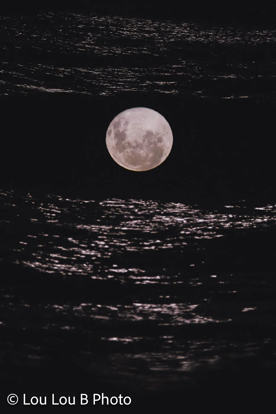 Full moon rising above dark ocean waves, with moonlight shimmering across the water.
