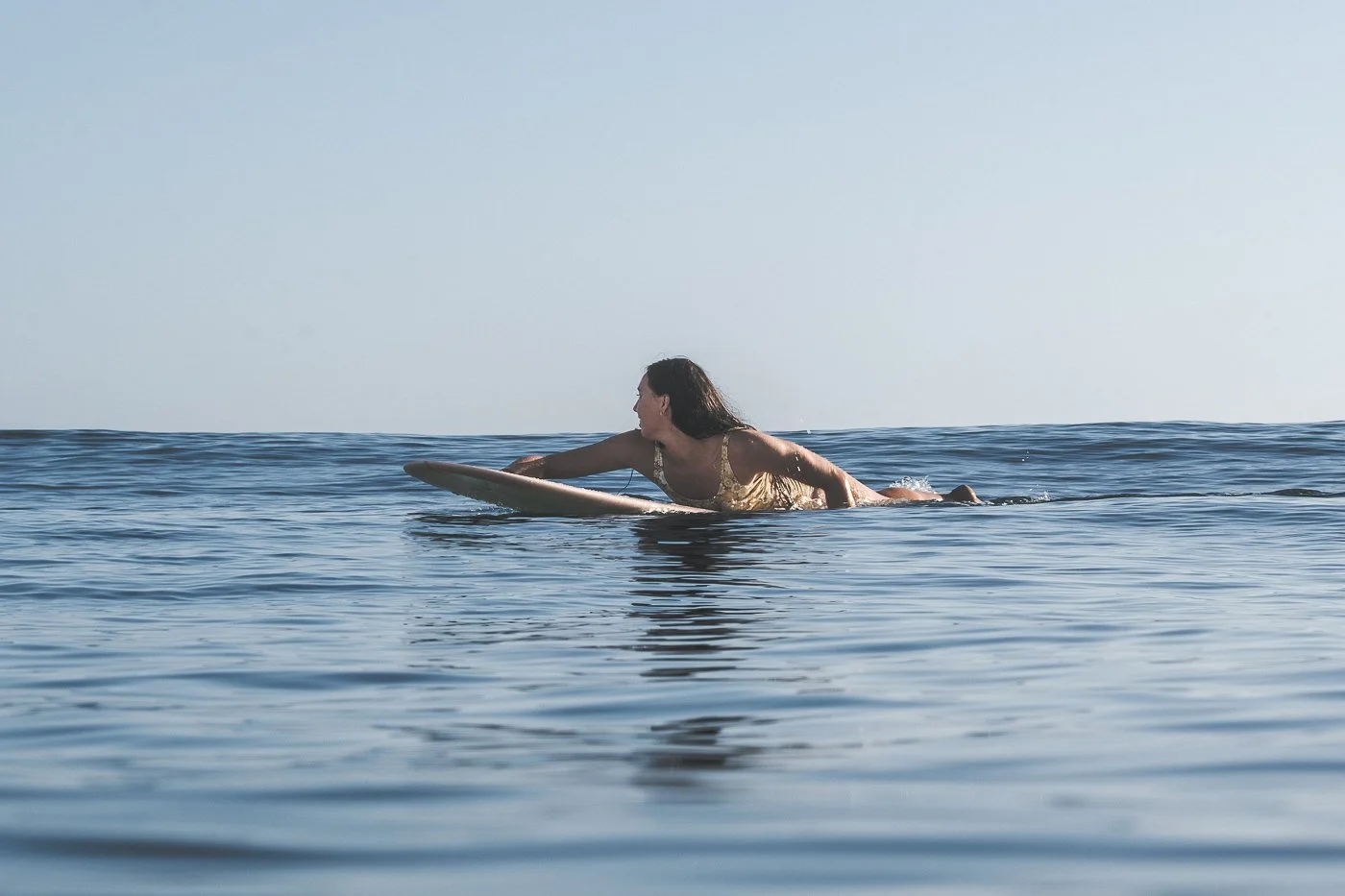 Woman paddling on a longboard in the calm blue ocean at Mount Maunganui, New Zealand.