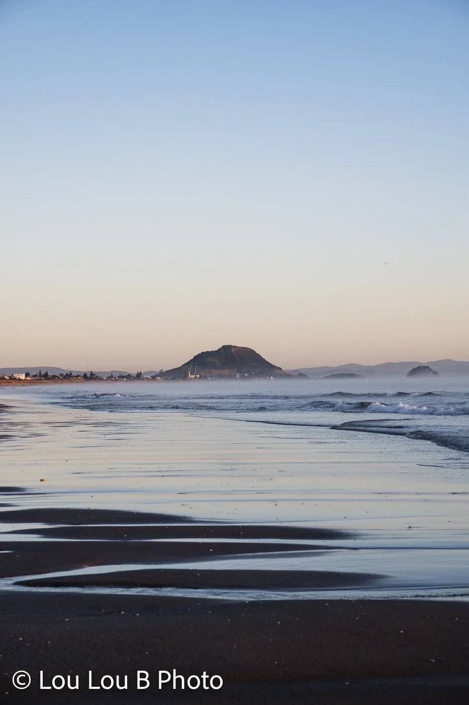 Mauao and Mount Maunganui coastline reflected in wet sand at sunrise