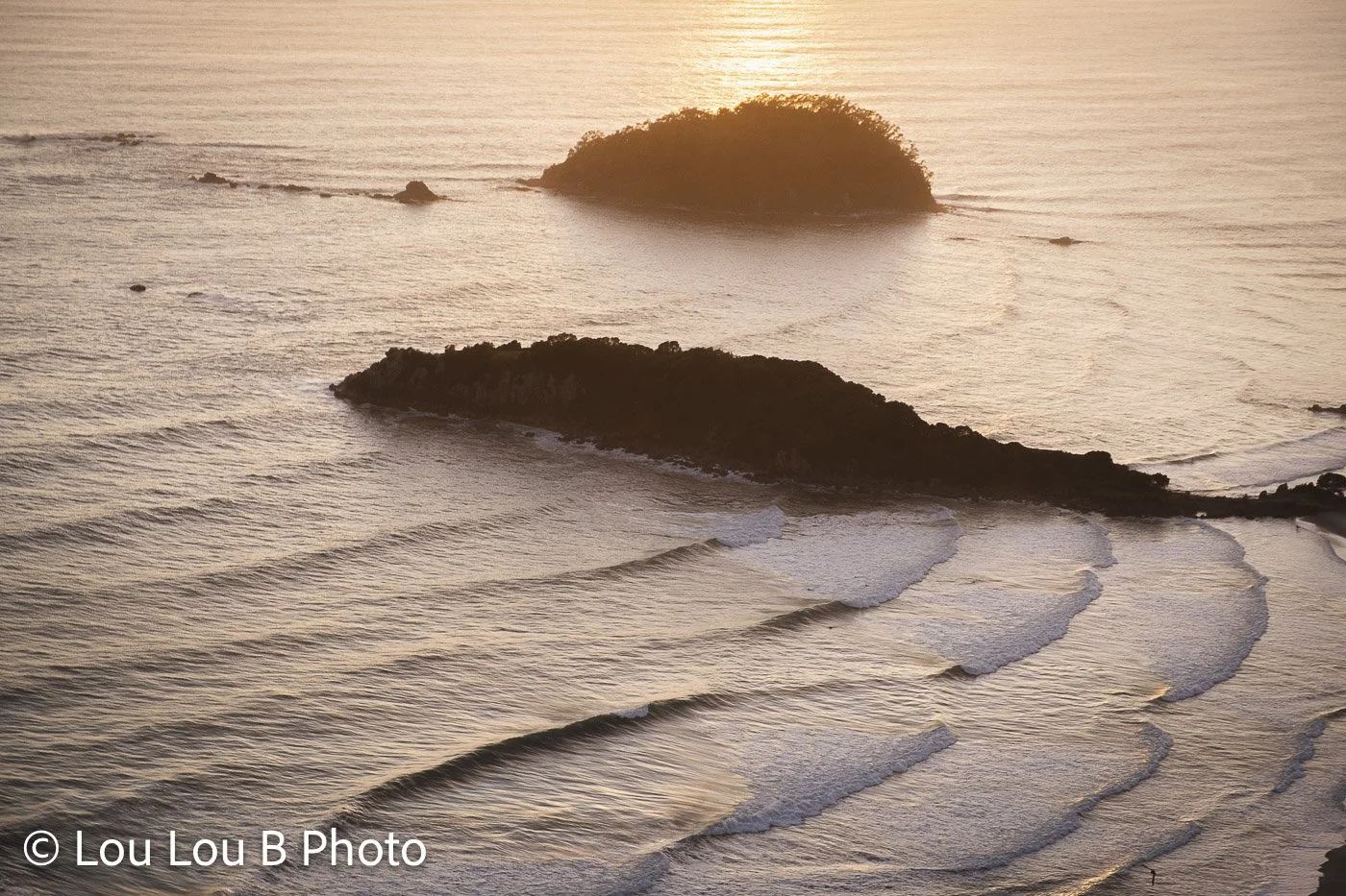 Golden coastal view of small rocky islands surrounded by gentle ocean waves in Mount Maunganui New Zealand.