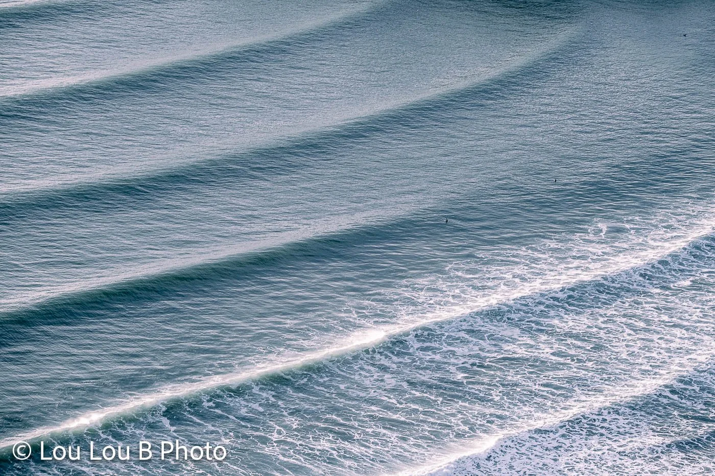 Elevated view of parallel ocean swell lines breaking into whitewater along the coast.