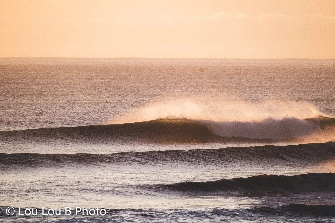 Clean ocean wave breaking with offshore spray illuminated by soft peach and golden light.