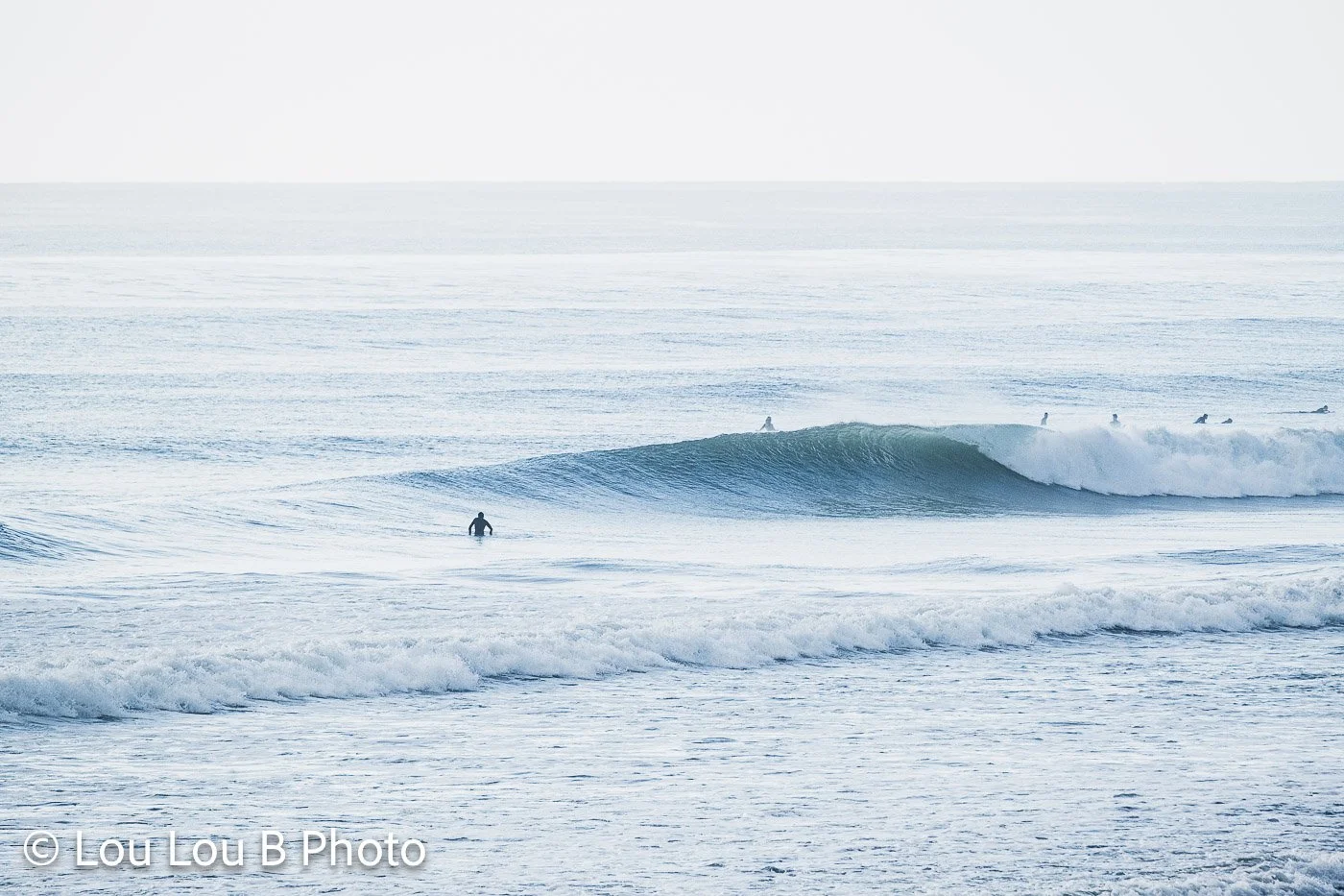 Surfers waiting among powerful blue ocean swell and breaking waves in bright coastal light.