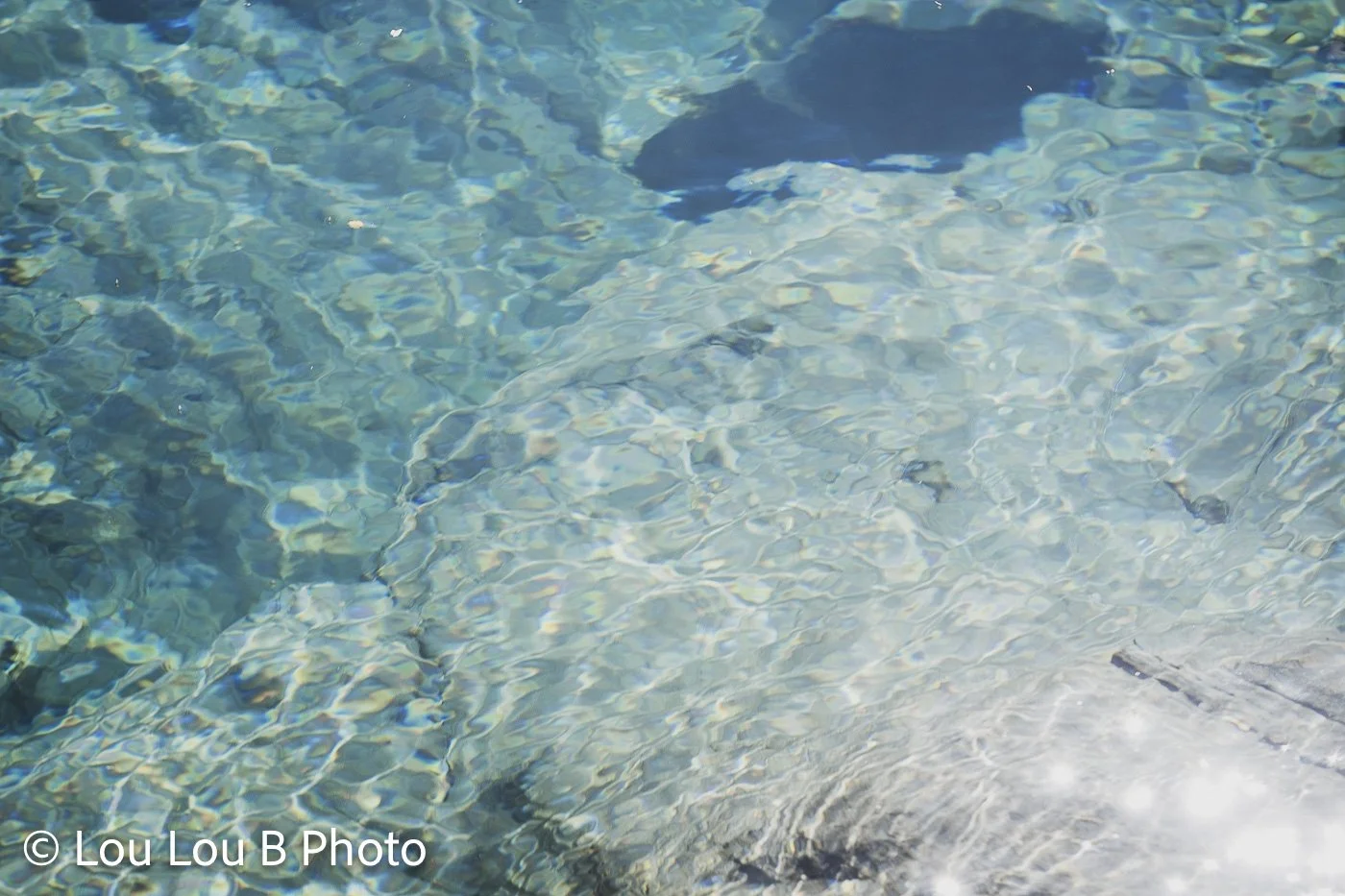 Clear shallow turquoise water with sunlight illuminating rocks beneath the surface.