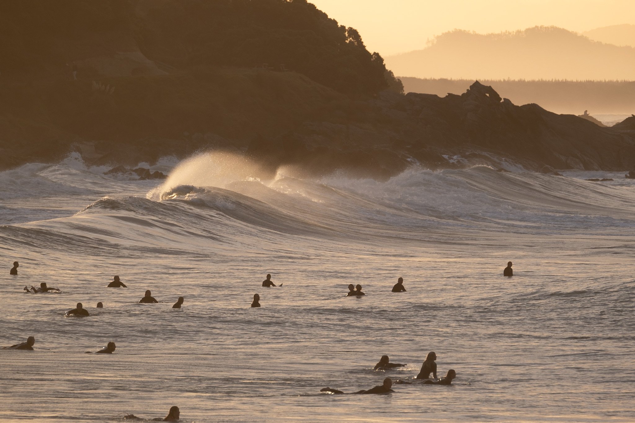 Powerful waves crash onto the shore of Mount Maunganui main beach in this photo taken from behind the scene on Leisure Island. The base of Mount Maunganui is silhouetted in the background, while surfers wait for the next wave to ride. A stunning view