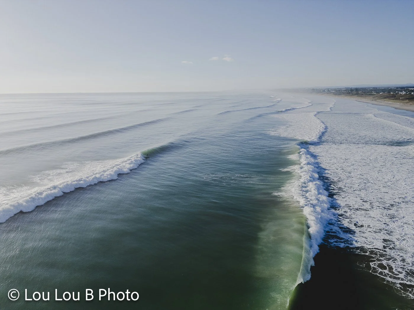 Aerial view of long ocean swell lines approaching a coastline in blue-green water.