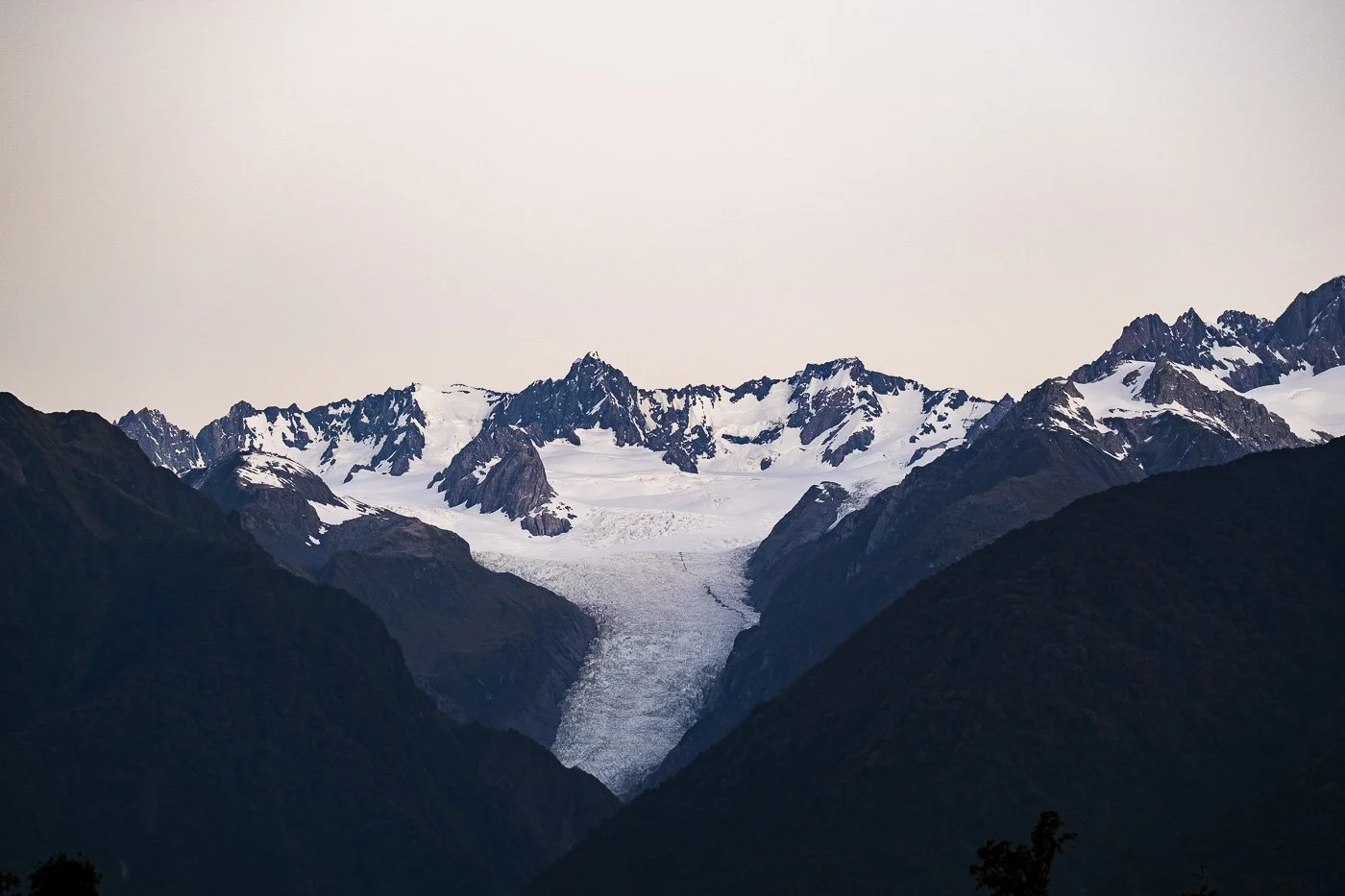 Fox Glacier flowing between snow-covered peaks and dark mountain ridges on the West Coast of New Zealand’s South Island.