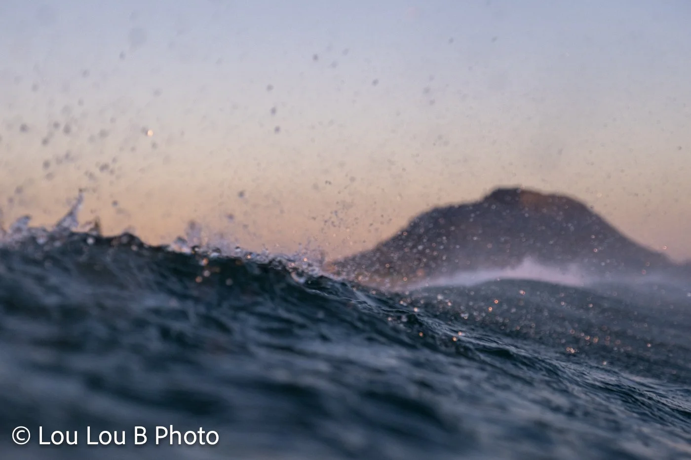 Ocean wave and sea spray with Mauao in the background at Mount Maunganui at sunrise