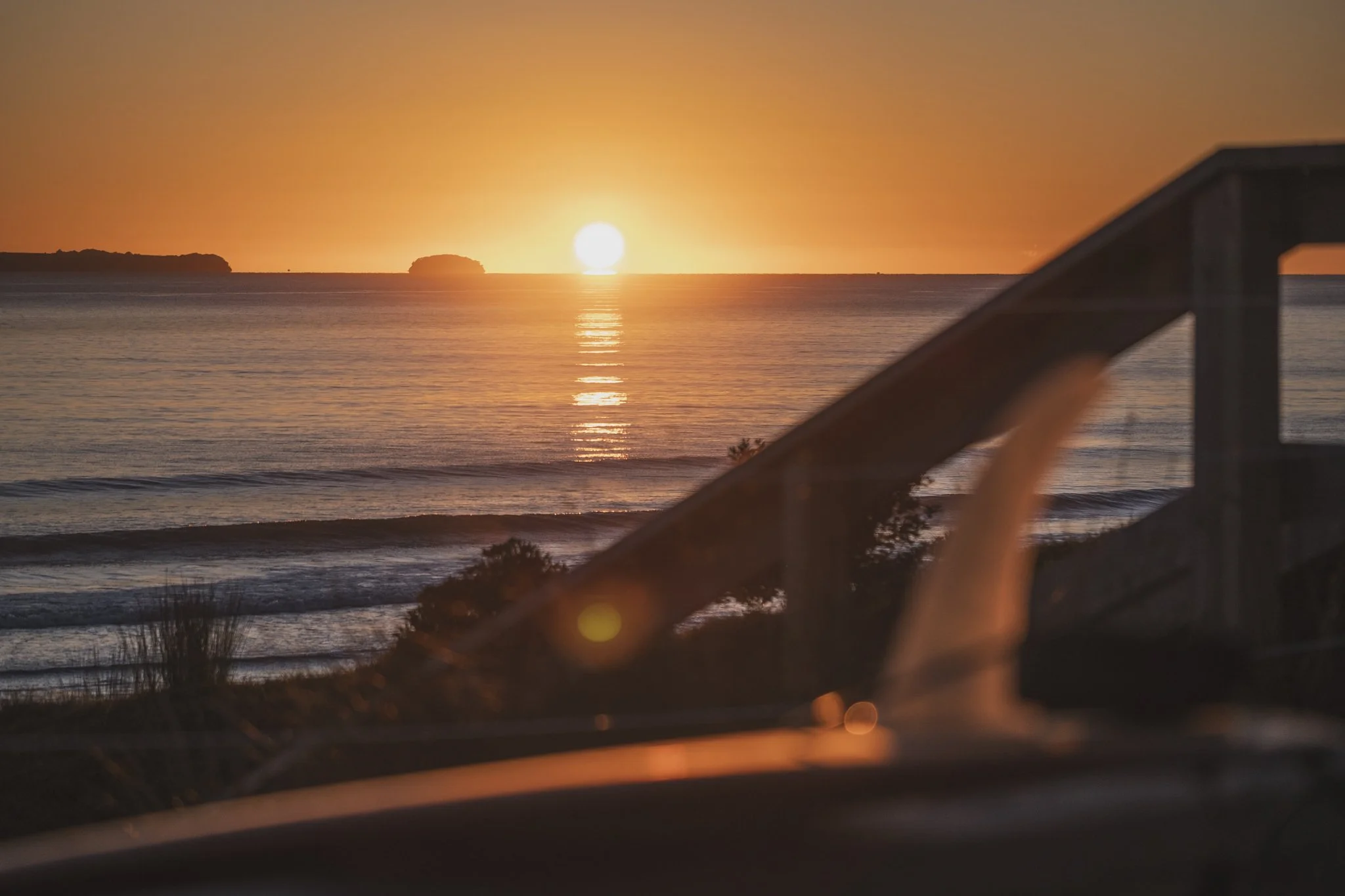 Golden orange sunrise over the ocean at Mount Maunganui, with the sun reflecting on the water and a beach access staircase in the foreground.