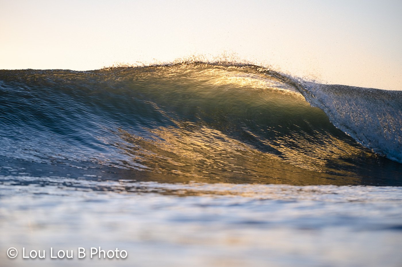 Translucent blue-green wave illuminated by warm golden sunlight as it breaks.