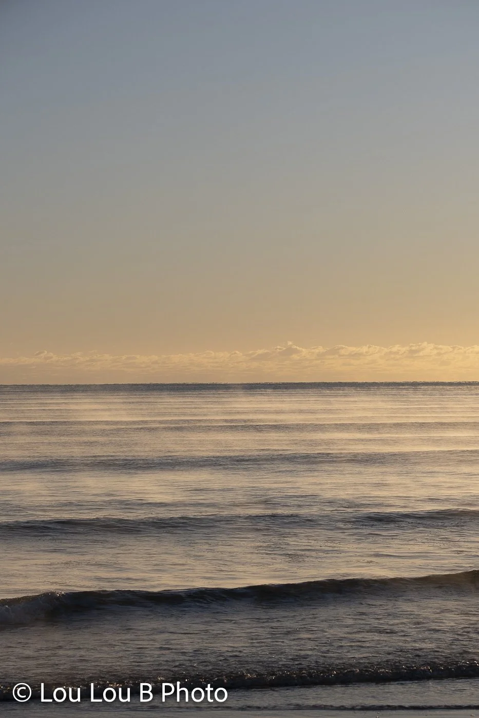 Soft ocean waves beneath a pale blue and warm cream horizon.