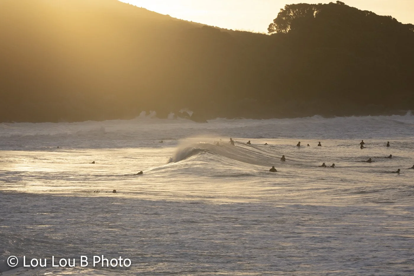 Surfers in golden ocean light beside Mauao at Mount Maunganui