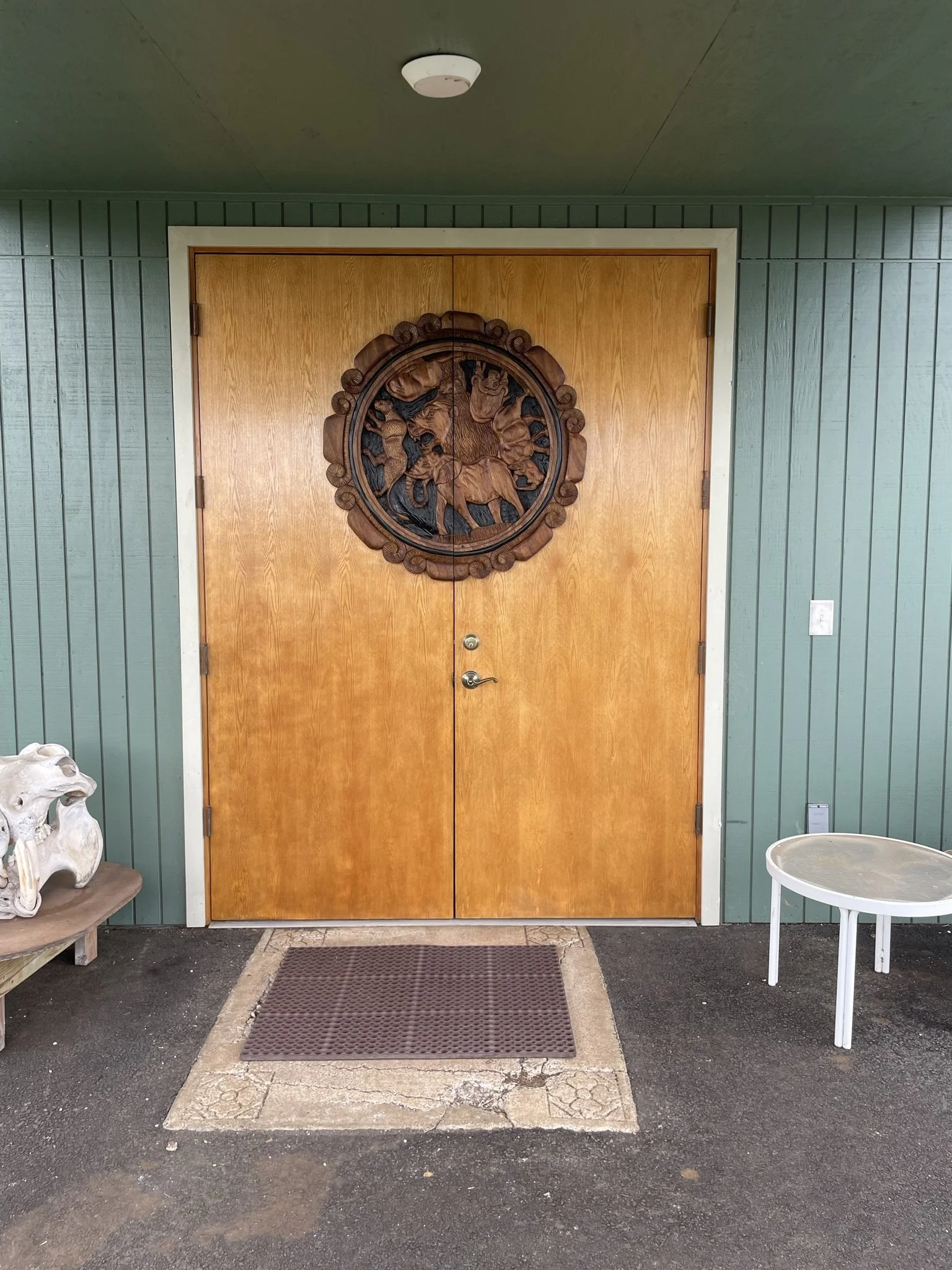 Hardwood door refinishing in a Maui home - wood door with a carved circular design, flanked by green panels, by Maui Home Refinishing.