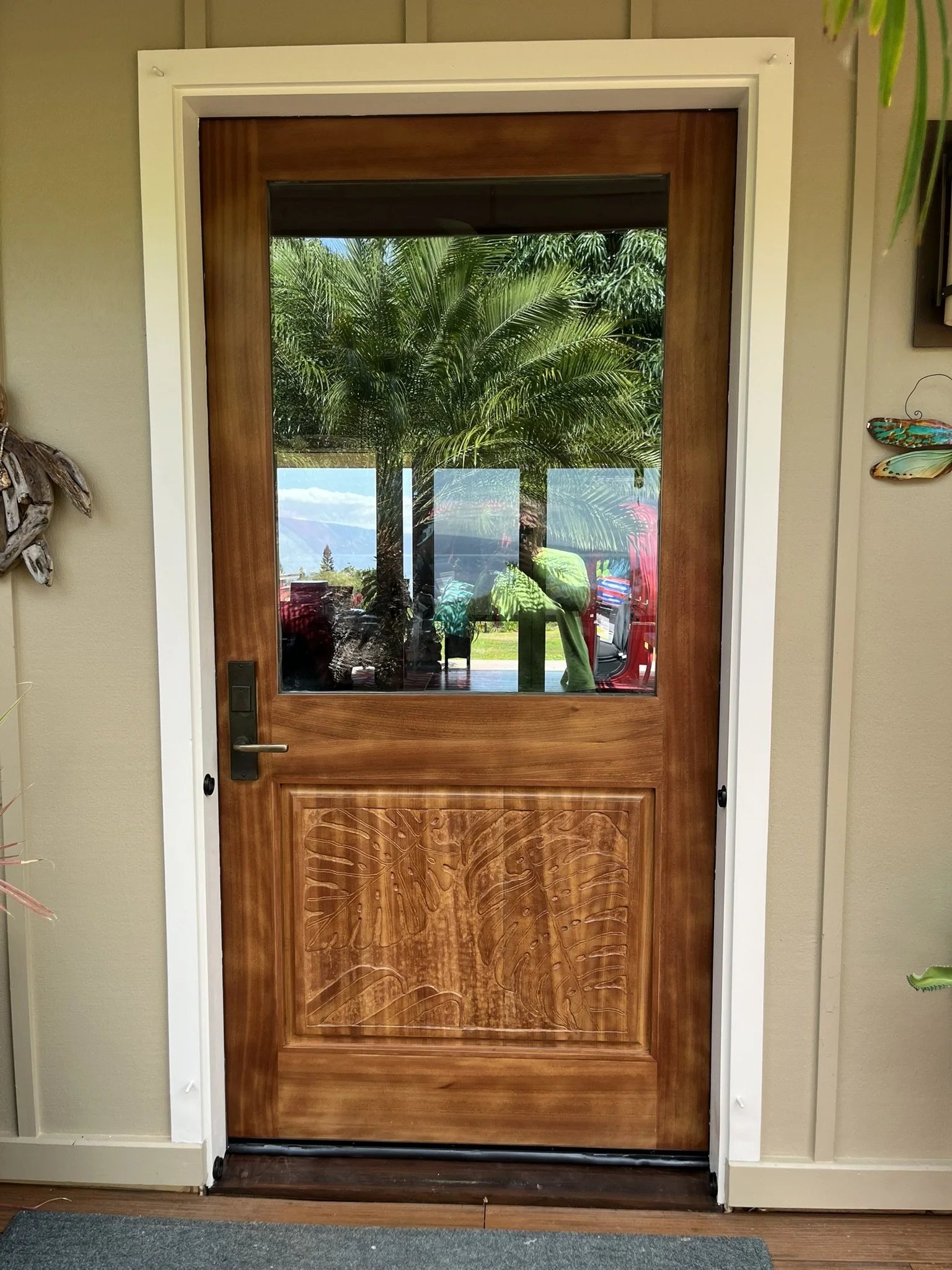 Hardwood door refinishing in a Maui home - wood door with glass panel reflecting outdoor trees and mountains, by Maui Home Refinishing.