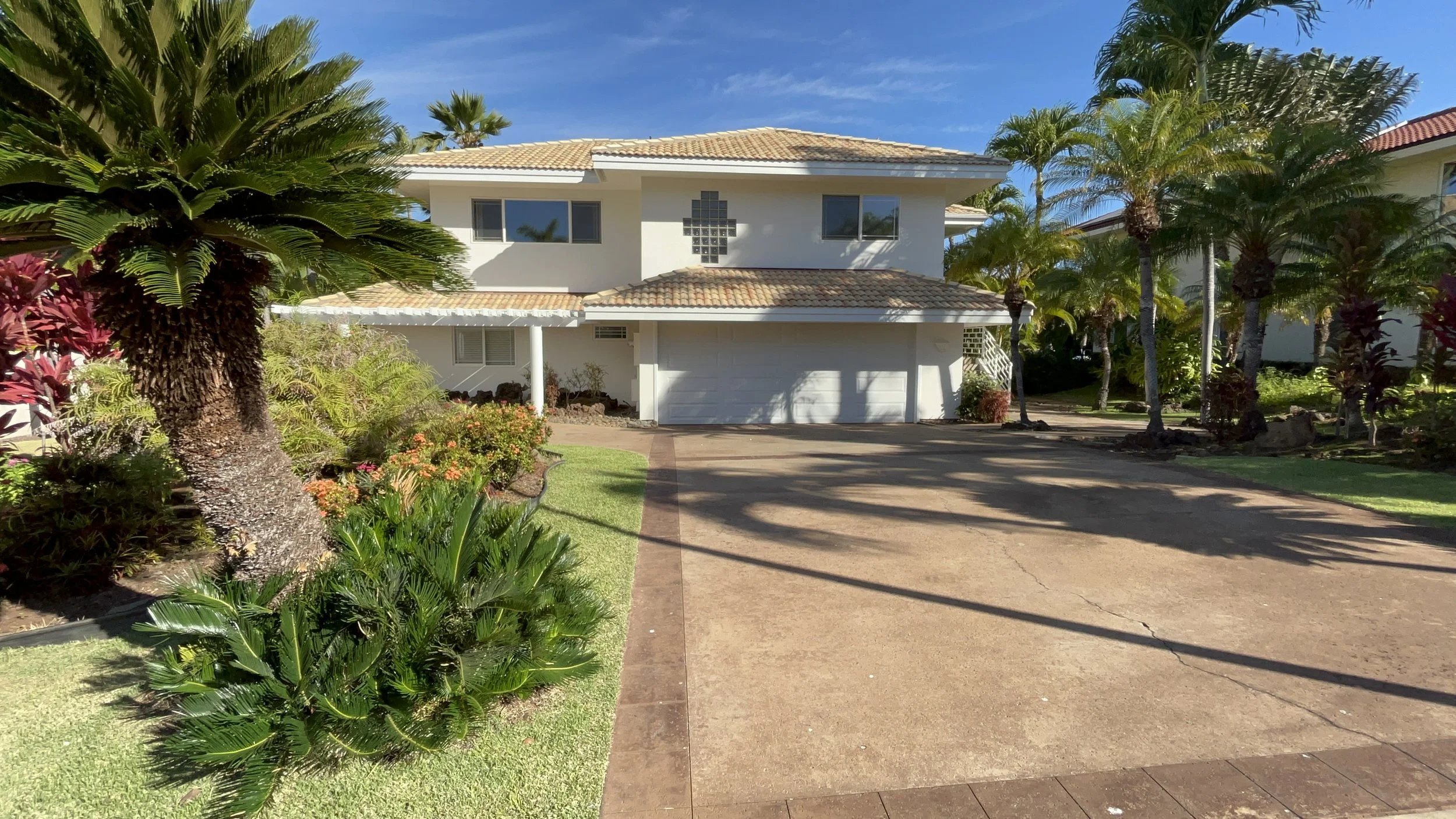 Exterior house painting in Maui - white two-story home with a tiled roof, surrounded by palm trees, by Maui Home Refinishing.