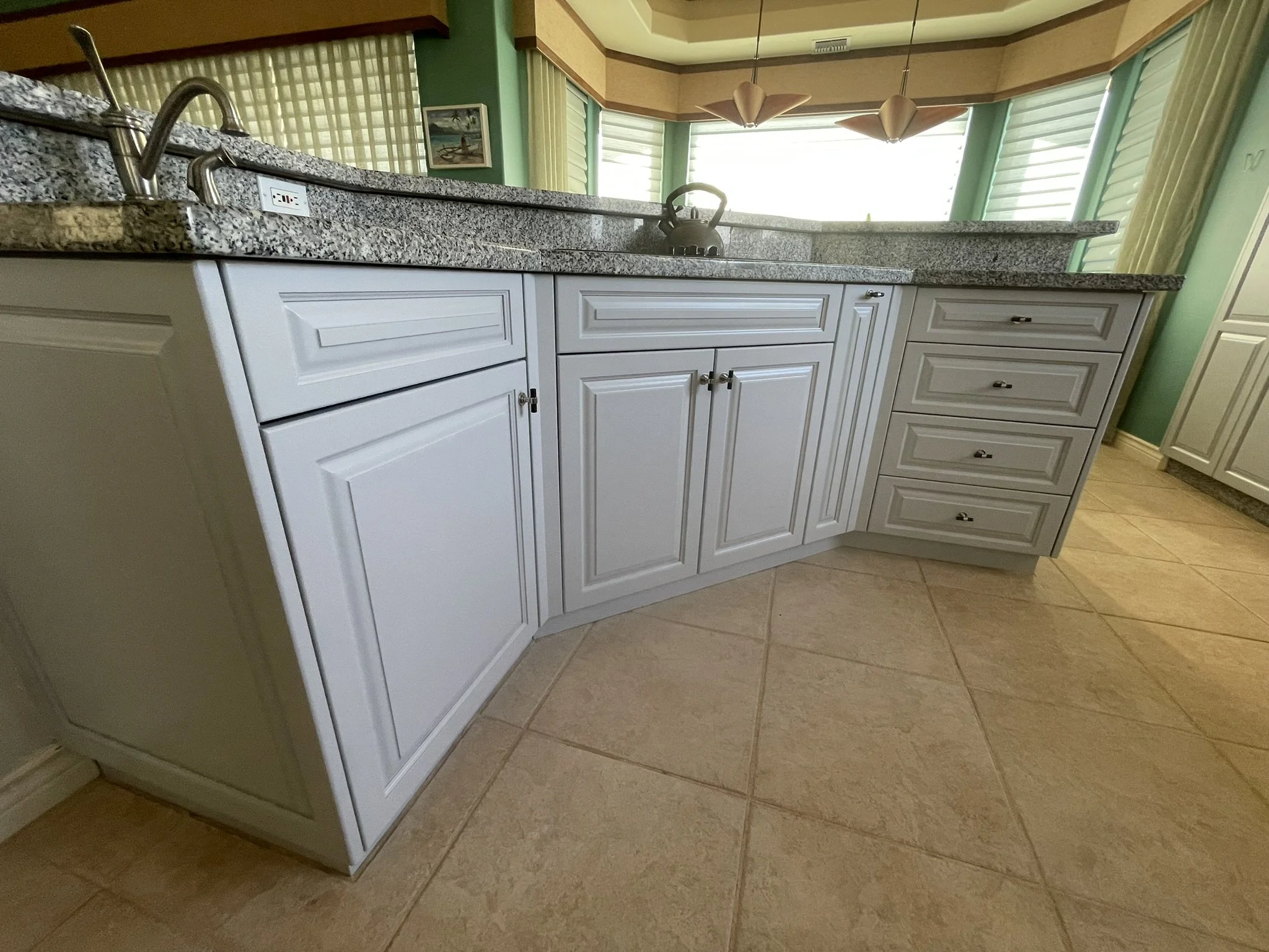Cabinet refinishing in a Maui home kitchen - white cabinets with granite countertops and tiled floor, by Maui Home Refinishing.