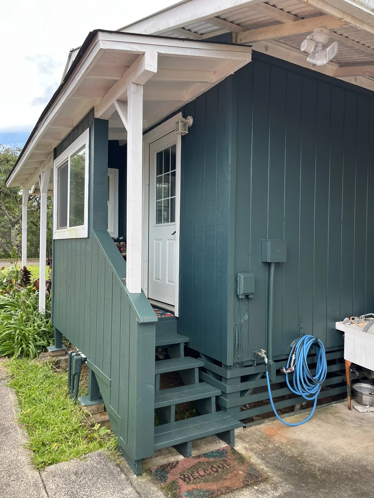 Exterior house painting in Maui - dark teal home with white door, covered porch, and staircase, by Maui Home Refinishing.