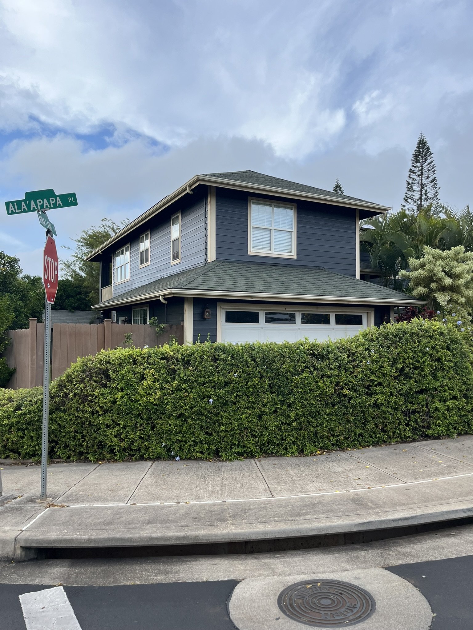 Exterior house painting on a Maui home - two-story house with blue siding, white trim, and a gray roof, by Maui Home Refinishing.