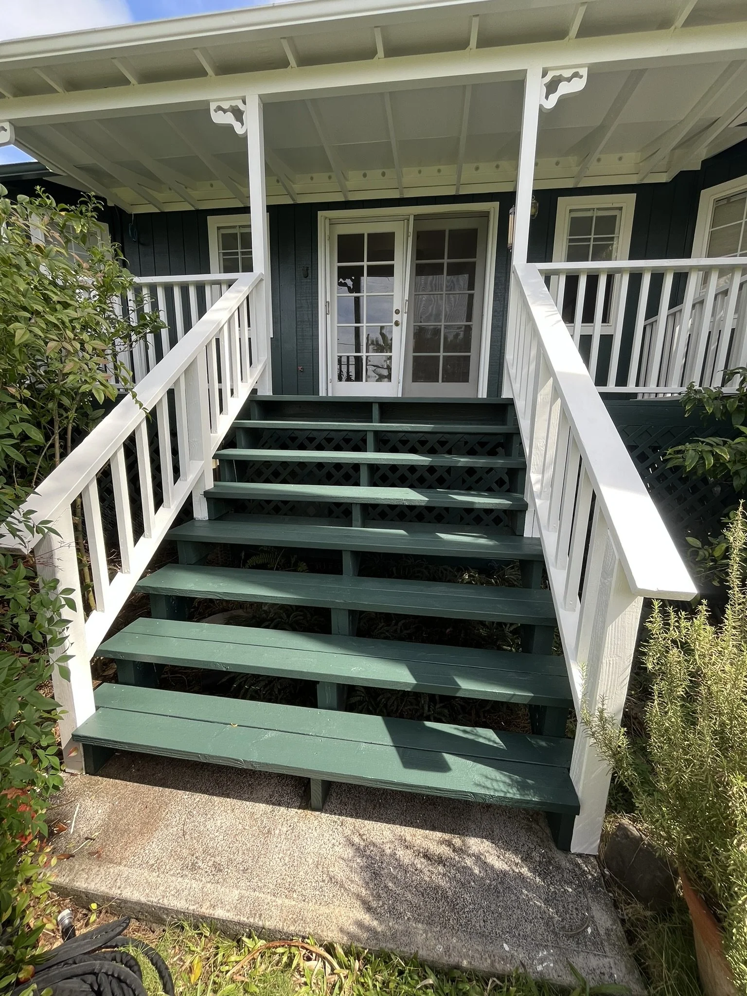 Exterior house painting in Maui - green wooden stairs and porch trim on a blue home, by Maui Home Refinishing.