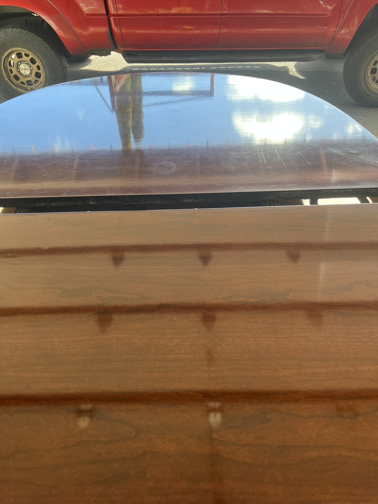 Wood furniture refinishing in a Maui home - reflective wood surface with a truck visible outside the window, by Maui Home Refinishing.