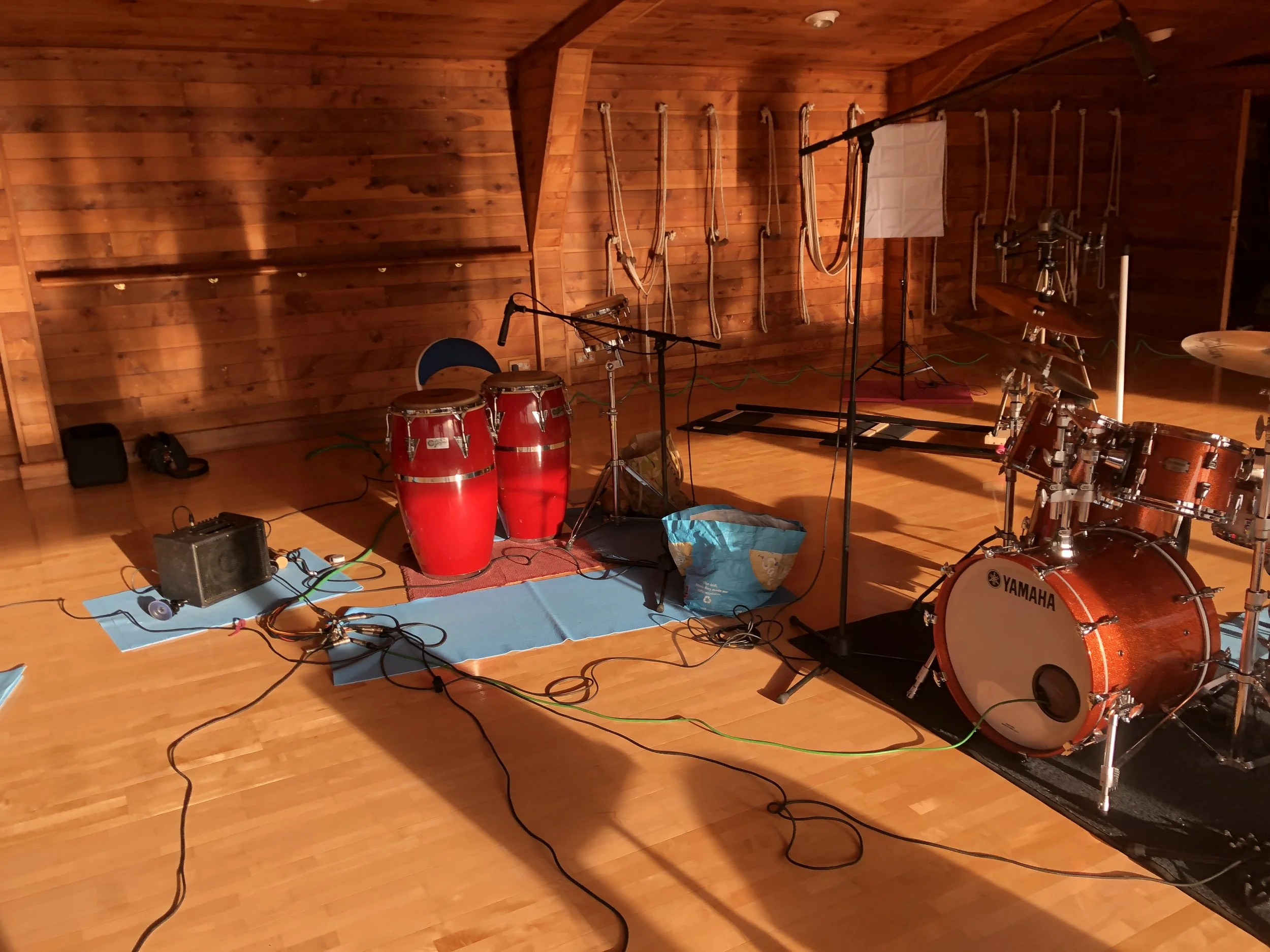 Music studio with percussion instruments, a microphone, and recording equipment on a wooden floor with warm lighting.