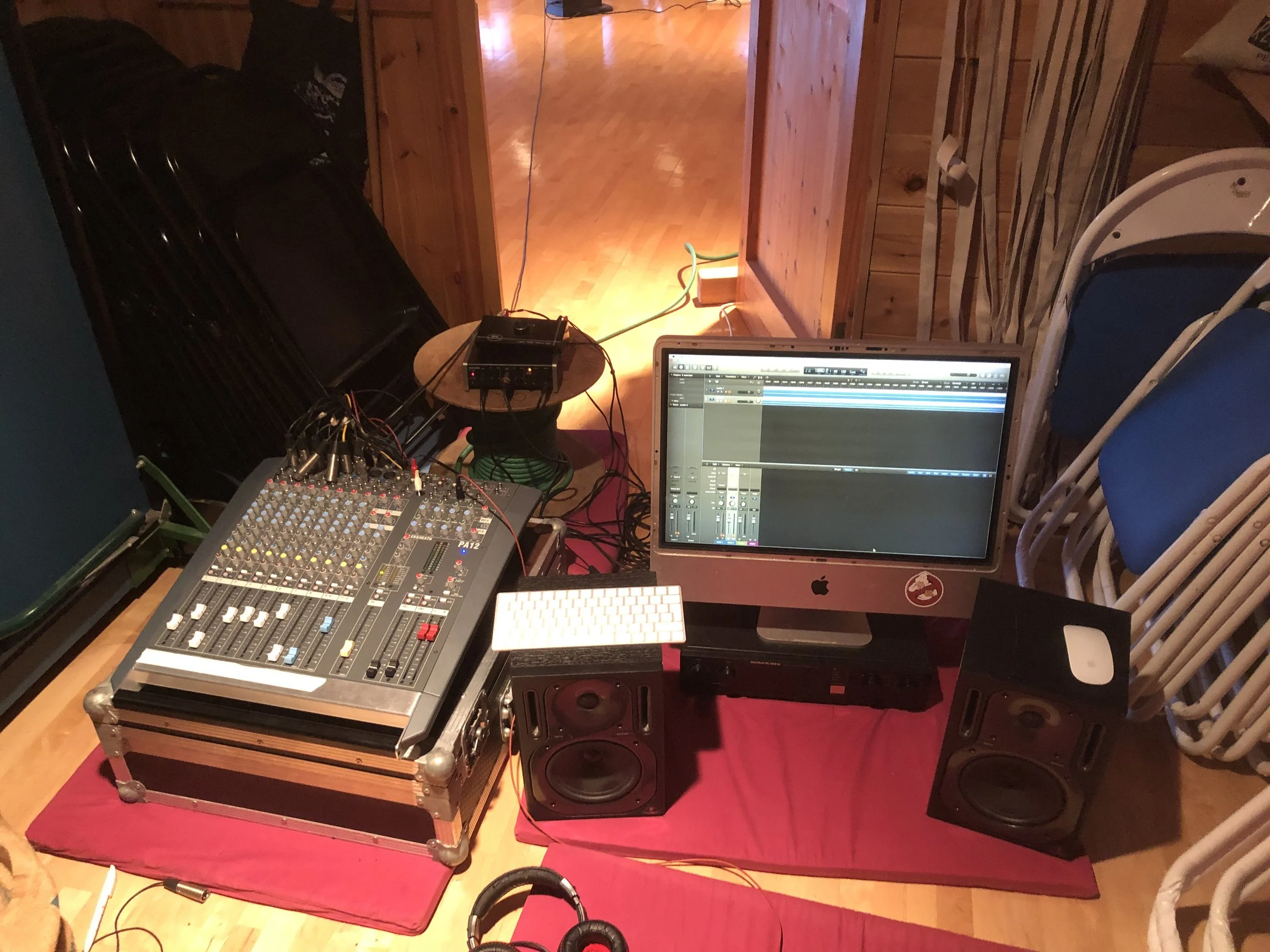 Music production setup with a mixing console, a computer displaying digital audio workstation software, studio monitor speakers, and various electronic equipment on a table covered with a red cloth.