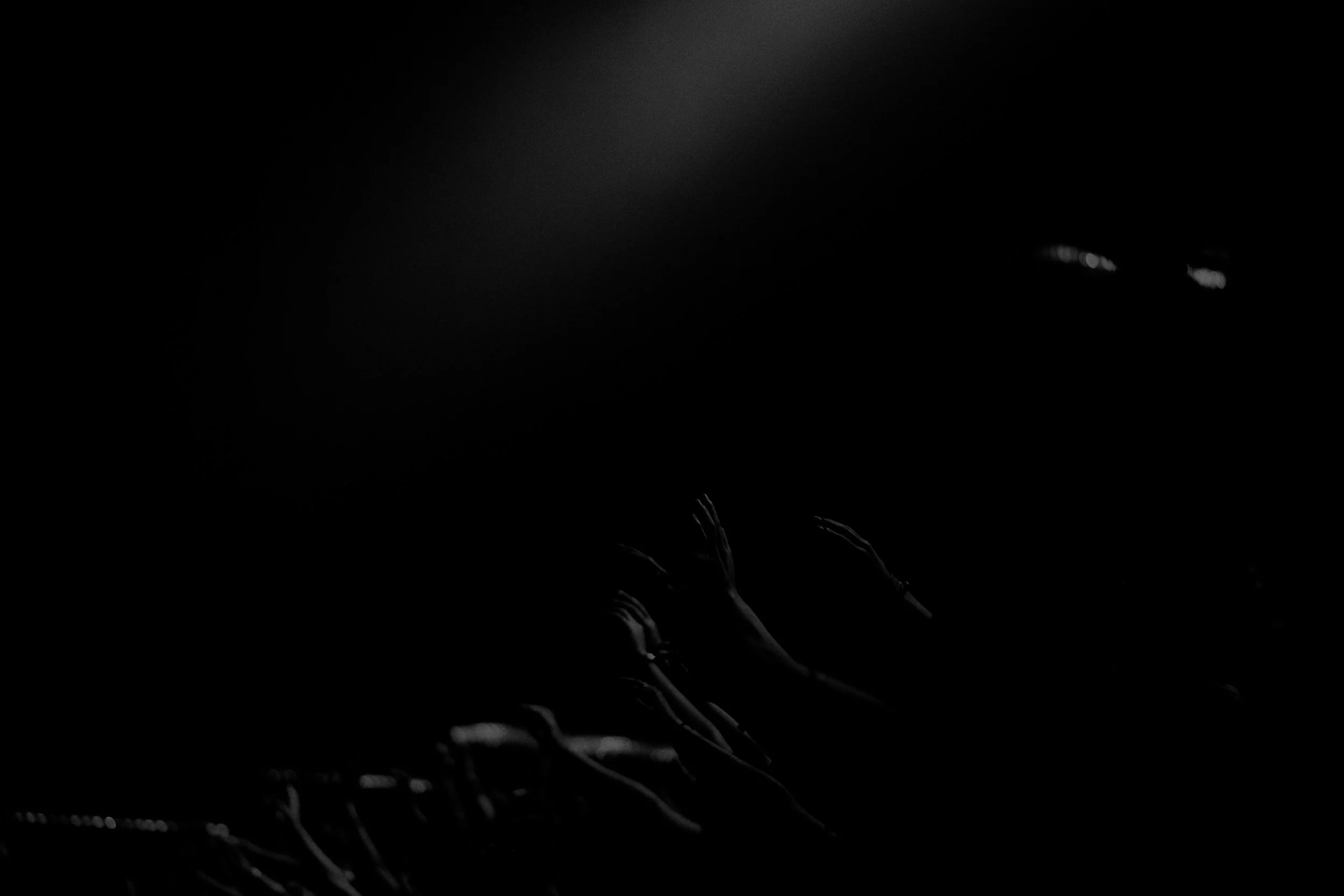 Dark image with indistinct outlines of hands reaching upward and faint light source in upper left corner.