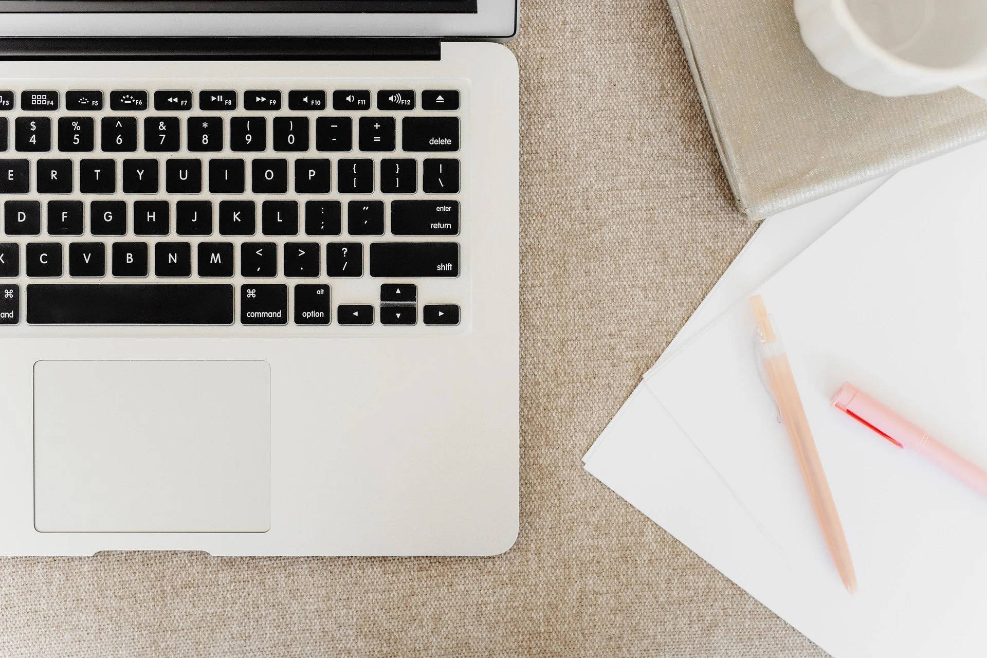 A close-up of an open macbook keyboard, pens, and note paper, representing an author's desk during a self-publishing coaching session