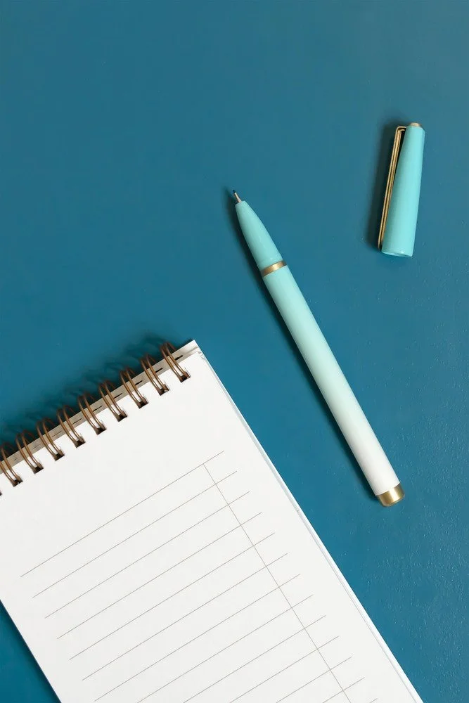 A spiral notebook and pen on a teal background representing a nonfiction author working with a book coach to find traditional publishing companies for first-time authors