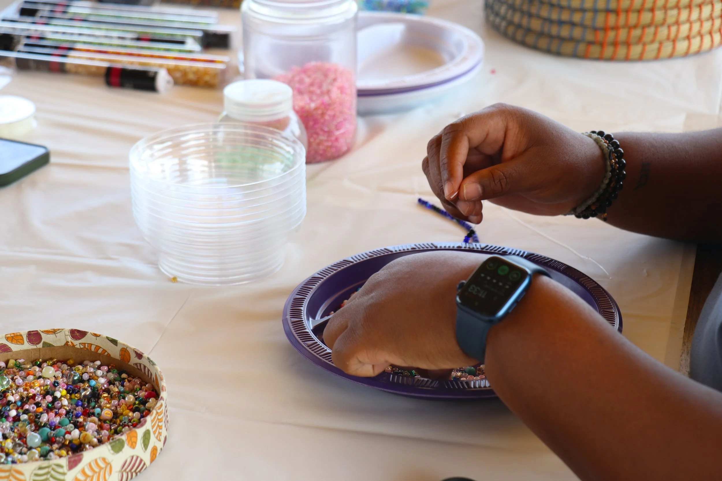 Person working on jewelry making with beads and tools on a table.