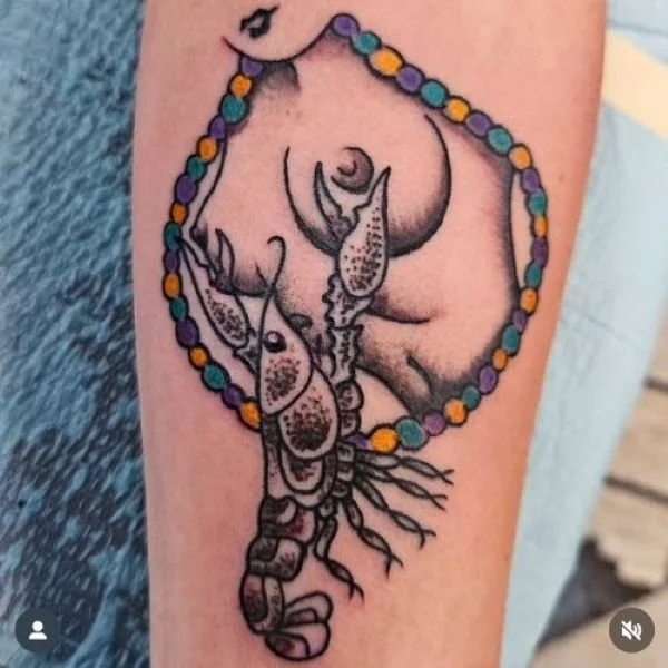 Tattoo of a crawfish pinching breasts with Mardi Gras beads