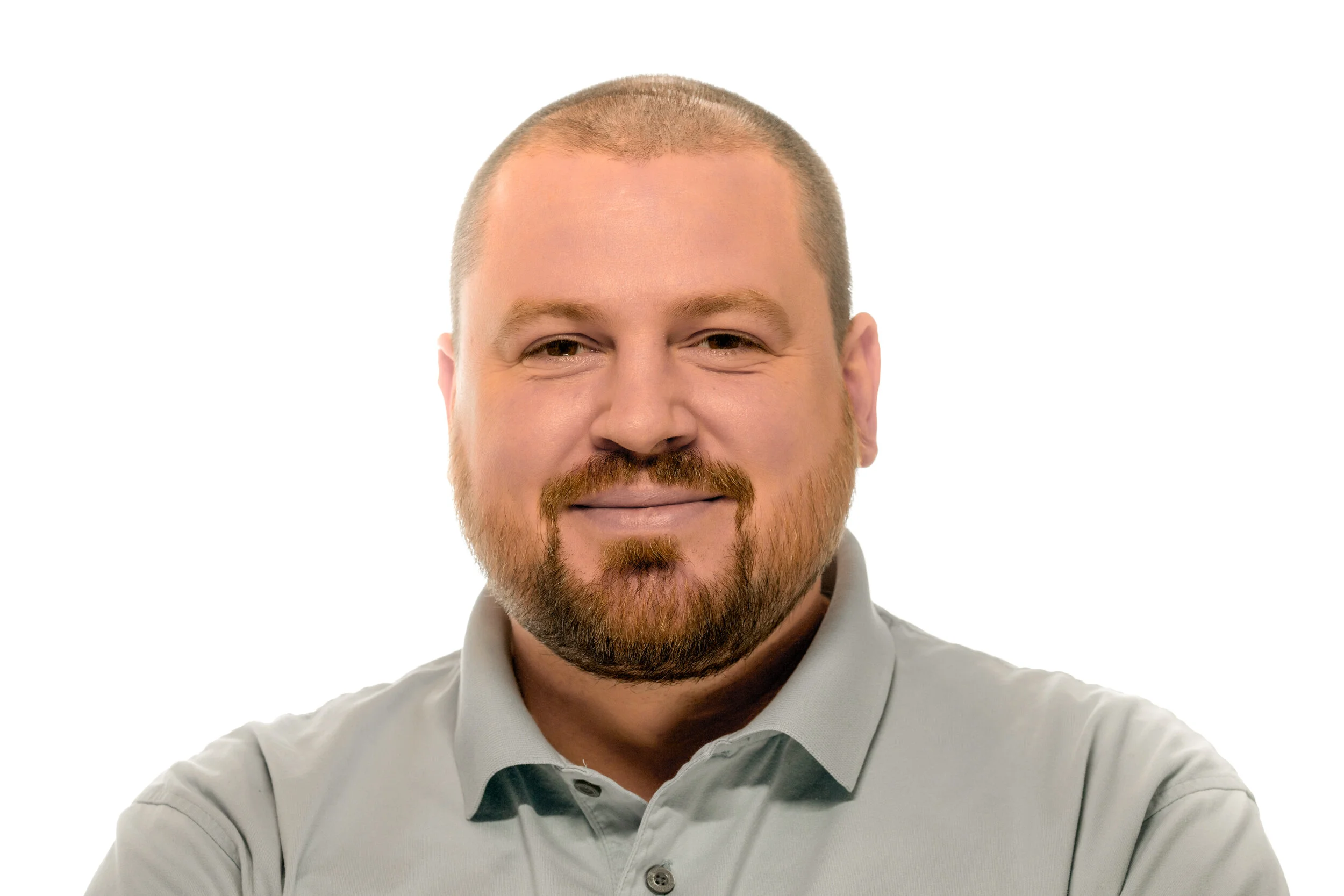 Headshot of a smiling man with short hair and a beard, wearing a light gray collared shirt, against a plain white background.