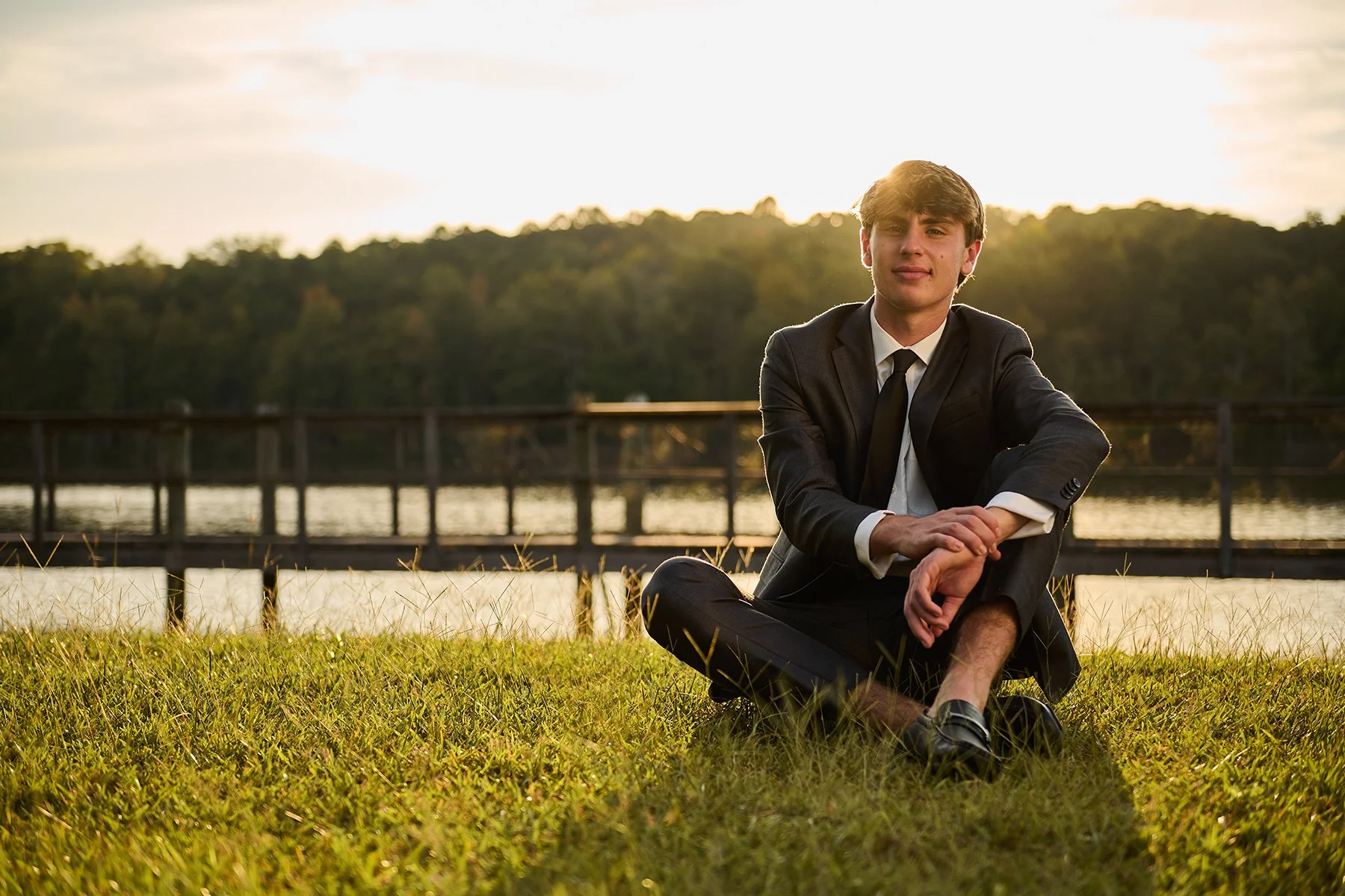 Boys senior portrait of a Class of 2027 guy in a suit sitting by the lake at sunset, photographed by South Atlanta Photography for senior sessions in Peachtree City and South Atlanta.