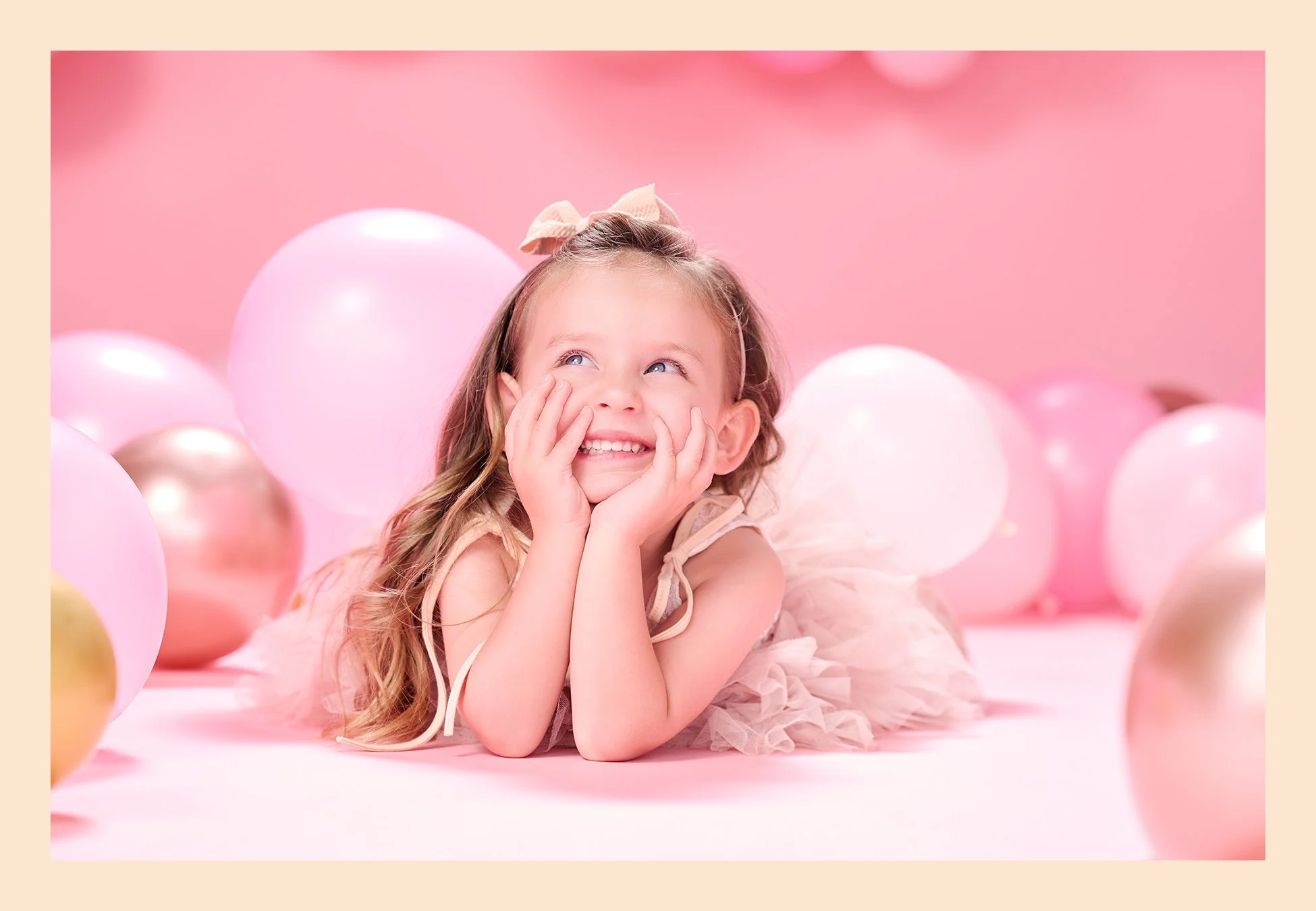 Four-year-old girl lying on a pink studio floor and smiling among pink, white, and metallic balloons during her fourth birthday portrait session.