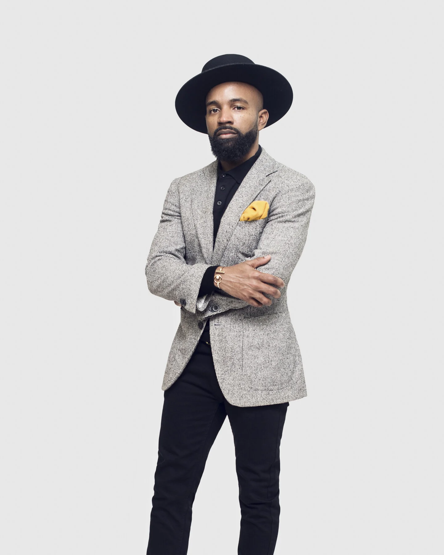 Full-length personal branding portrait of a male creative professional in a blazer and hat photographed against a clean studio background for business and marketing content.