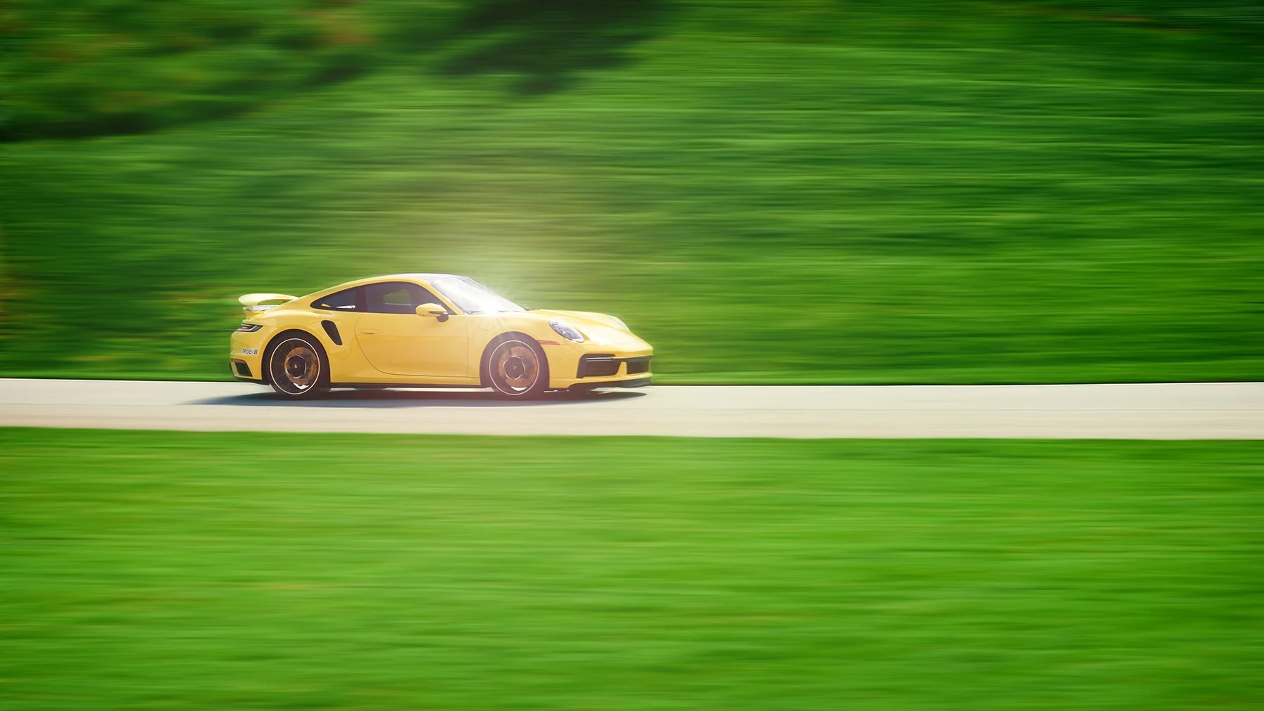 Commercial automotive photography of a yellow Porsche 911 Turbo captured in motion with a blurred green background, emphasizing speed and performance.