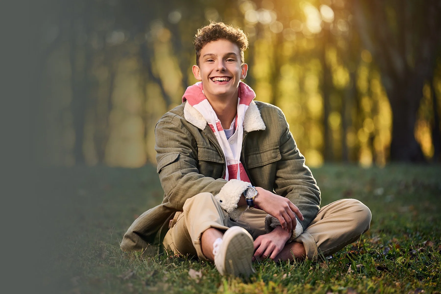 Senior guy sitting casually outdoors and smiling in warm fall light during a relaxed senior portrait session in Peachtree City, Georgia.