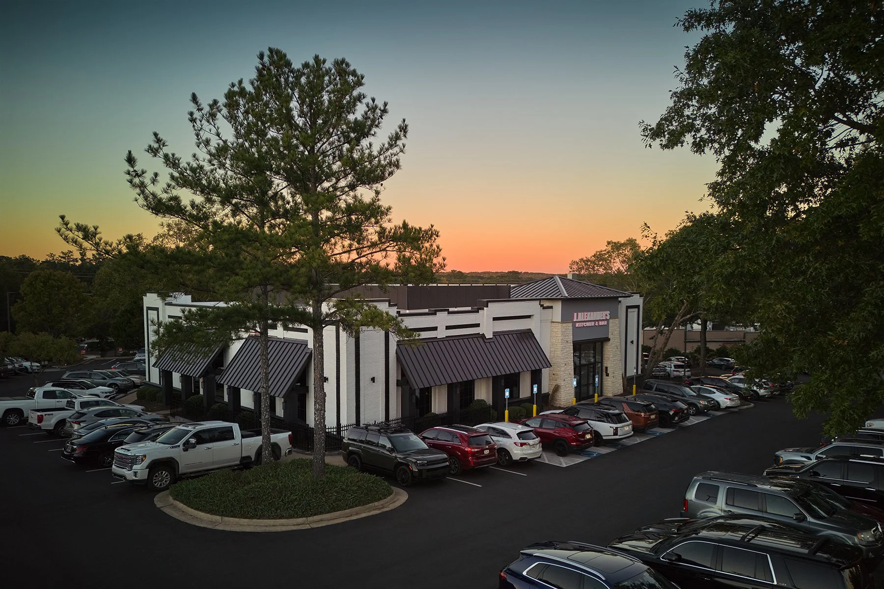 Elevated drone photograph of J. Alexander's restaurant, its active parking lot, and sunset sky in Peachtree City, Georgia, by South Atlanta Photography.